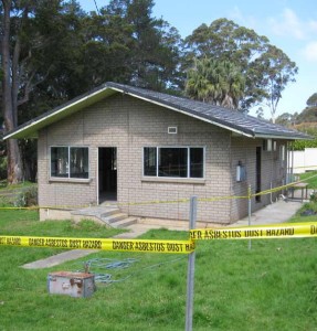 Photo looking at building being prepared to have Asbestos removed, surrounded by yellow danger tape.